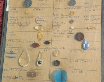 May include: A close-up of a beige card with various glass and metal buttons, beads, and other small objects. The card is labeled with descriptions and measurements for each item. The card is divided into sections with different categories of items, such as "wolf", "Tobe Art", and "House of B".