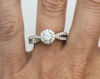 May include: A diamond engagement ring with a halo setting and a double band. The ring is set in white gold and features a round brilliant cut diamond.