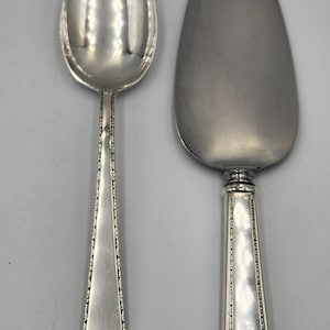 May include: A set of two silver serving pieces, a spoon and a cake server, with a decorative border pattern on the handles.