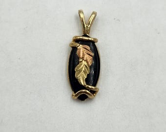 May include: A gold pendant with a black oval center featuring three gold-colored leaves. The pendant has a gold bail and is likely made of gold-filled or plated metal. The leaves are detailed with veins and textures.