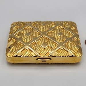 May include: A gold-colored metal cigarette case with a woven pattern.