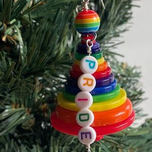 May include: A rainbow-coloured Christmas tree bauble made of stacked buttons with the word "PRIDE" spelled out in white letters.