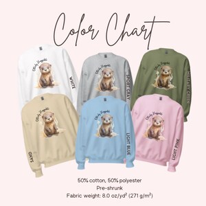May include: Color chart showing ten different sweatshirt colors with an otter graphic and the text "Otterly Huggable". The colors are white, sport gray, military green, sand, light blue, light pink.