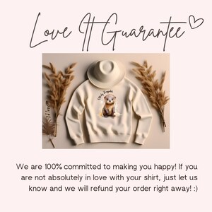 May include: A cream-colored sweatshirt with a brown otter graphic and the text "Cutiely Naggable". The sweatshirt is laid flat on a light brown surface with dried grass.