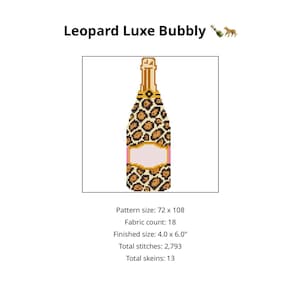 May include: A cross-stitch pattern of a champagne bottle with a leopard print design. The bottle has a gold top and a pink label. The text "Leopard Luxe Bubbly" is at the top. Finished size is 10.16 x 15.24 cm.