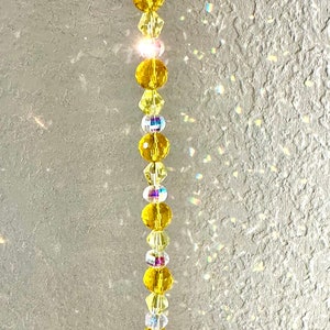 Puede incluir: Un charm de pato de goma amarillo cuelga de una cadena de cuentas de cristal. Las cuentas son transparentes y amarillas, y la cadena está unida a un anillo plateado.