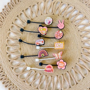 May include: A collection of colorful shoe charms with a retro, hippie theme. Designs include a peace sign, a rainbow, a butterfly, a flower, and the words "Love", "Peace Love", "Stay Groovy", and "Flower Power".