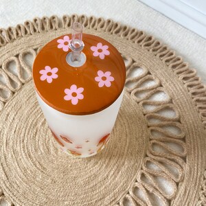 May include: A frosted glass tumbler with a brown lid featuring pink flowers. The tumbler has a straw and a floral design.