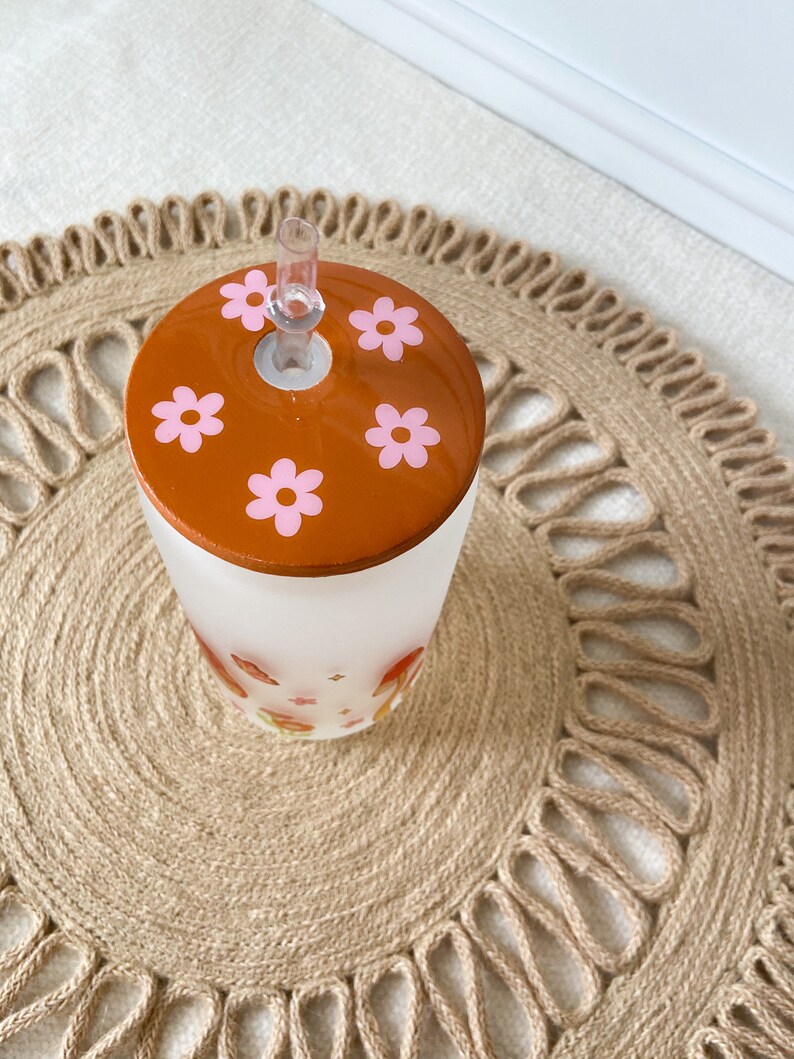 May include: A frosted glass tumbler with a brown lid featuring pink flowers. The tumbler has a straw and a floral design.