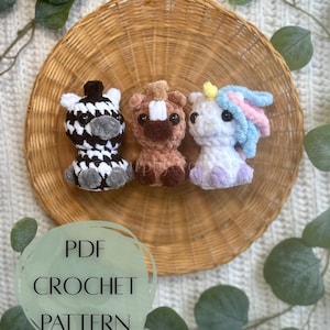May include: Three crocheted animal figures: a zebra, a horse, and a unicorn. The zebra is black and white, the horse is brown, and the unicorn is white with a blue and pink mane. The image also includes text that says "PDF CROCHET PATTERN".