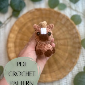May include: A crocheted horse figurine in shades of brown, tan, and white. The amigurumi horse has large black eyes and a small, light-colored mane. The image includes the text "PDF CROCHET PATTERN".
