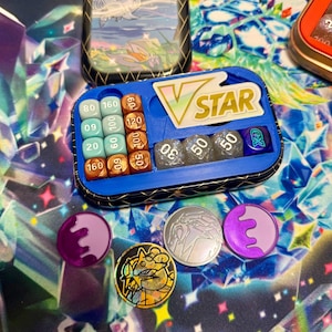 Könnte beinhalten: Ein blau-schwarzer Organizer mit Würfeln, Münzen und Metalldosen. Der Organizer trägt den Text "V STAR". Die Würfel sind in verschiedenen Farben und haben Zahlen. Die Münzen sind lila, silber und gold.