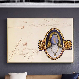 May include: Abstract art print featuring a woman's portrait with a blue face and gold hair, set within an oval frame. The artwork is in a gold frame and hangs above a brown leather sofa. A white coffee table holds decorative items.