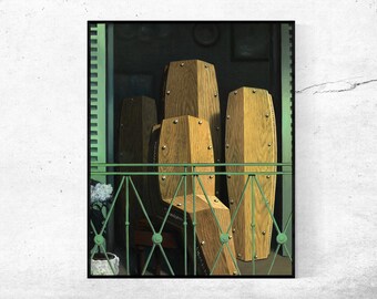 Puede incluir: Una impresión artística que presenta varios ataúdes de madera con tachuelas metálicas, dispuestos en un balcón con una barandilla verde. Los ataúdes son de color marrón claro y el fondo es verde oscuro.