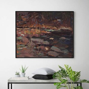 Peut inclure: Peinture à l'huile encadrée de noir représentant une scène de rivière avec de l'eau sombre et des rochers. L'œuvre utilise une palette de bruns, de verts et de bleus pour représenter le paysage naturel. Le tableau est au-dessus d'une table en béton avec des plantes et des coussins.