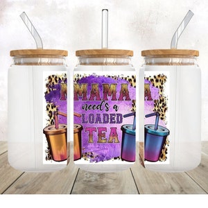 May include: Three clear glass tumblers with lids and straws. Each tumbler has a purple, pink, and white sticker with the text "Mama needs a loaded tea" and a graphic of a beverage with a straw. The background is a blurred image of a wooden surface.