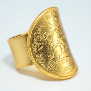 May include: Gold ring with a gold coin featuring a depiction of a horse and rider, with the text "THE SILVER STATE" and "2006" on the coin.