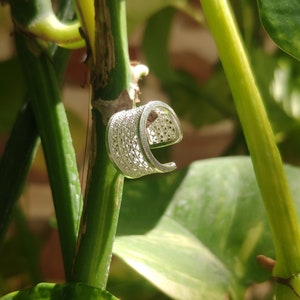 Puede incluir: Un anillo de plata con un diseño delicado e intrincado. El anillo está hecho de metal tejido y tiene una forma curva.