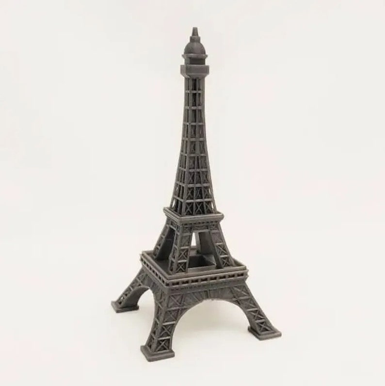 Op de afbeelding: Een donkergrijze miniatuur van de Eiffeltoren, een gedetailleerde replica van het iconische Parijse monument. De toren heeft ingewikkeld traliewerk en een puntige torenspits, staand op een vierkante basis. Een decoratief souvenir.