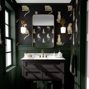 May include: A dark green bathroom with a black and white cheetah print wallpaper. A dark brown vanity with a white marble countertop and a gold faucet. A mirror with a gold frame hangs above the vanity. Two gold wall sconces with white glass shades are on either side of the mirror.