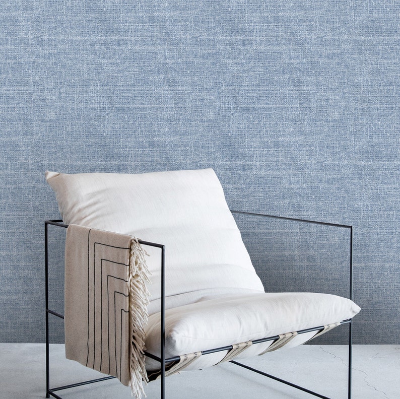 May include: A white chair with a black metal frame and a white cushion. The chair is sitting in front of a blue textured wall.