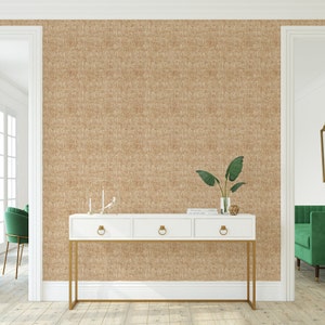 May include: A white console table with gold metal legs and three drawers. The table is placed in front of a wall with a brown textured wallpaper. A green plant and a decorative object are on top of the table.