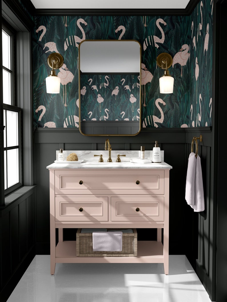 May include: A bathroom with a pink vanity, gold fixtures, and a marble countertop. The walls are dark green with a flamingo pattern wallpaper. A gold-framed mirror hangs above the vanity, and a white towel hangs on a gold ring.