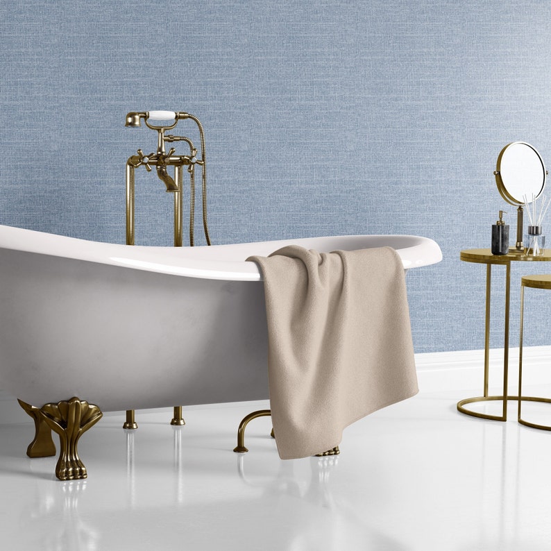 May include: A white clawfoot bathtub with gold-toned fixtures and a beige towel draped over the edge. The bathtub is in a bathroom with a blue textured wall and a gold-toned side table with a mirror and toiletries.
