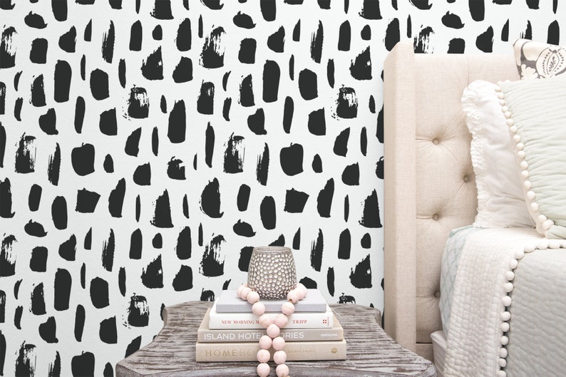 May include: Black and white abstract brushstroke pattern wallpaper with a white headboard and bed with white bedding and a pink and white throw pillow.