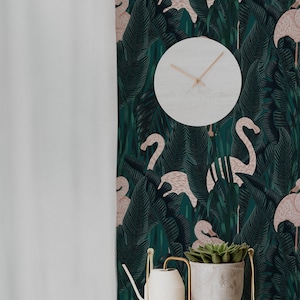 May include: A white round clock with light brown hands hangs on a wall with a dark green flamingo and tropical leaf pattern. A white shelf holds a white watering can and a gray pot with a green succulent.