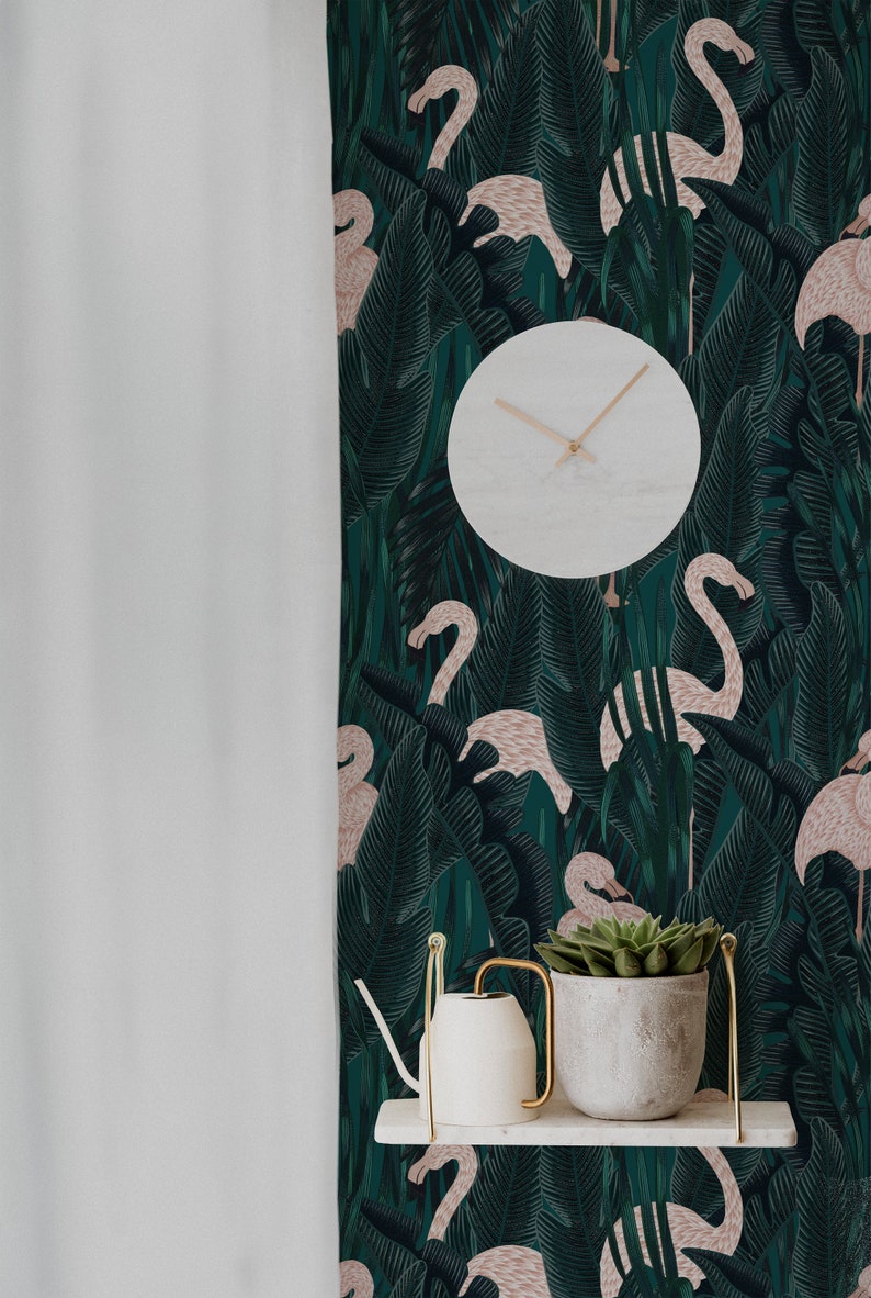 May include: A white round clock with light brown hands hangs on a wall with a dark green flamingo and tropical leaf pattern. A white shelf holds a white watering can and a gray pot with a green succulent.