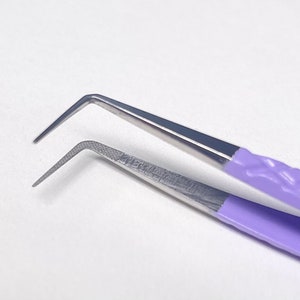 May include: A pair of angled tweezers with a purple rubberized handle. The tweezers are made of stainless steel and have a fine tip.