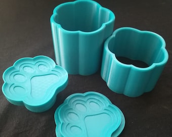 May include: Three teal blue 3D printed paw print shaped containers. Two are cylindrical and one is a flat lid. The lids have a raised paw print design.
