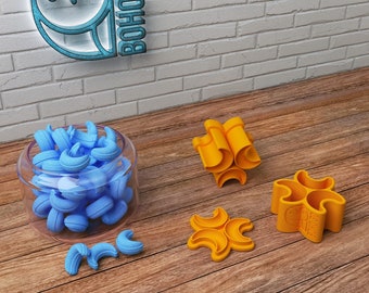 May include: A set of four yellow plastic cookie cutters shaped like crescent moons. The cutters are arranged on a wooden surface. There is a glass jar filled with blue plastic crescent moon shapes in the background.