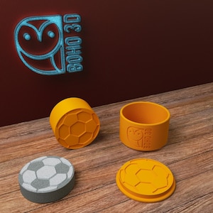 Könnte beinhalten: Vier orangefarbene und graue 3D-gedruckte Behälter mit einem Fußball-Design. Die Behälter sind mit "BOHO 3D" beschriftet.