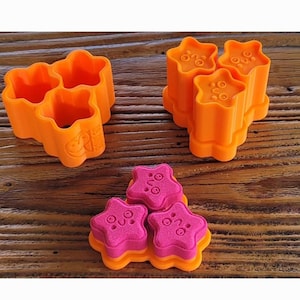 Puede incluir: Tres moldes de estrella de color naranja con un diseño en relieve de "O". Tres moldes de estrella de color rosa con un diseño en relieve de "O".