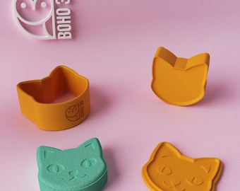 May include: Four cat-shaped cookie cutters in orange and teal green, with a white owl logo and the text "BOHO 3D" on a pink background. One orange cutter is a 3D shape, while the others are flat. The cat faces have simple features.