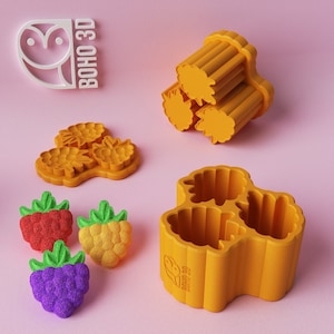 May include: Three orange silicone molds for making candy or soap in the shape of raspberries. The molds are arranged in a triangle shape. The molds are labeled "BOHO 3D".