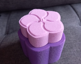 May include: A purple flower-shaped box with a pink flower-shaped lid. The box is made of a textured material.