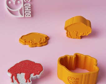 May include: Four 3D printed cookie cutters in the shape of a buffalo. Two are yellow, one is red, and one is yellow with the text "BOHO 3D" on the side.