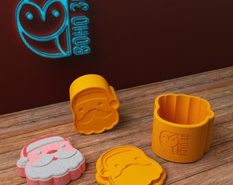 May include: Four yellow plastic cookie cutters shaped like Santa Claus. The cutters are on a wooden surface. The cookie cutters are for making Christmas cookies.