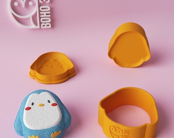 May include: Four orange plastic cookie cutters in the shape of a penguin. The penguin has a round body, a small beak, and two small wings. The cutters are on a pink surface. The text "BOHO 3D" is on one of the cutters.