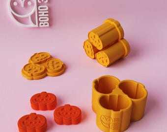 May include: A collection of orange and yellow 3D-printed Halloween-themed items. Includes pumpkin-shaped cookie cutters, pumpkin shapes, and a logo that says "BOHO 3D". The items are arranged on a pink background.