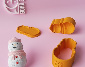 May include: A set of three orange plastic cookie cutters shaped like a snowman. The cutters are on a pink surface. The cutters have the text "BOHO 3D" on them.