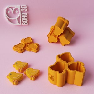 May include: Three yellow silicone molds shaped like chicks, with a logo that says "BOHO 3D". There are also three yellow chick-shaped cookies.