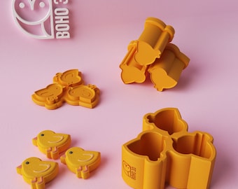 May include: Three yellow silicone molds shaped like chicks, with a logo that says "BOHO 3D". There are also three yellow chick-shaped cookies.