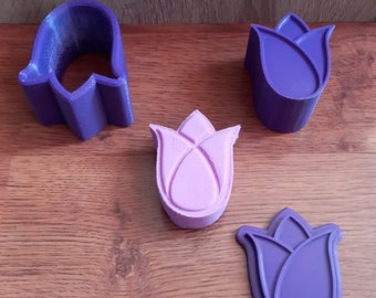 May include: Four purple and pink plastic tulip-shaped cookie cutters on a wooden surface.