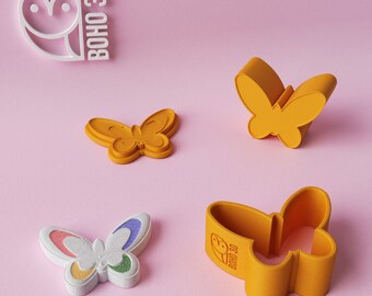 May include: Four 3D printed butterfly cookie cutters. Two are solid orange, one is white with rainbow accents, and one is orange with the logo "BOHO 3D" on the side.
