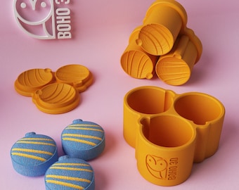 May include: A collection of 3D-printed items in shades of yellow and blue, set against a pink background. The items include containers, lids, and decorative spheres with yellow stripes. The "BOHO 3D" logo is also visible.