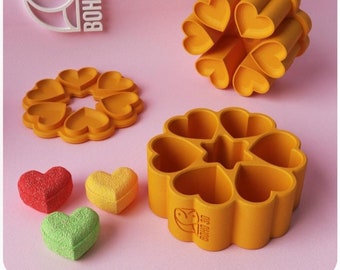 May include: A set of six yellow heart-shaped molds for making candy or soap. The molds are arranged in a circle and have a Boho 3D logo on the bottom. There are three heart-shaped candies in different colors: red, yellow, and green.